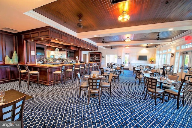 dining space with wooden ceiling, a ceiling fan, a bar, beamed ceiling, and crown molding