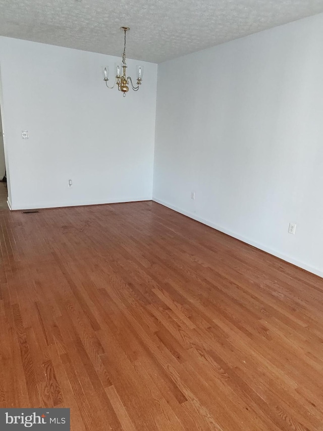 spare room featuring hardwood / wood-style floors, a chandelier, and a textured ceiling