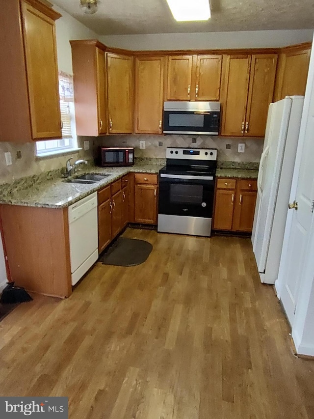 kitchen with light stone counters, light wood-style flooring, stainless steel appliances, a sink, and brown cabinets