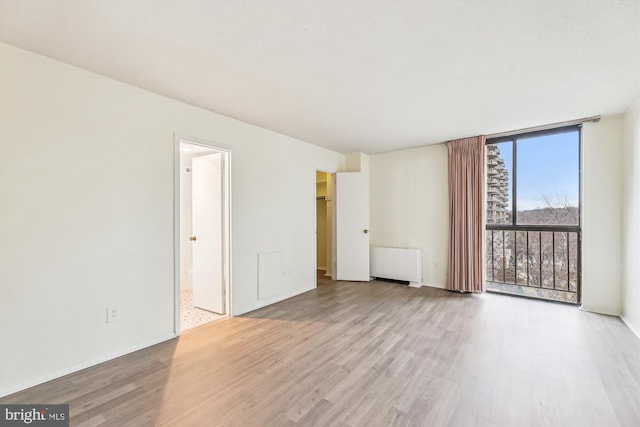 unfurnished room featuring radiator, baseboards, floor to ceiling windows, and wood finished floors