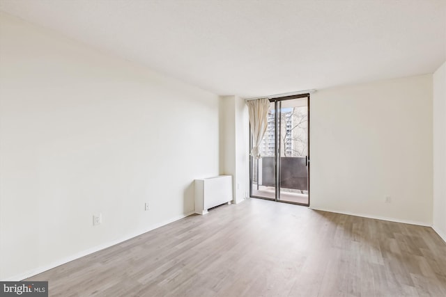 empty room featuring light wood-style floors, radiator heating unit, and a wall of windows