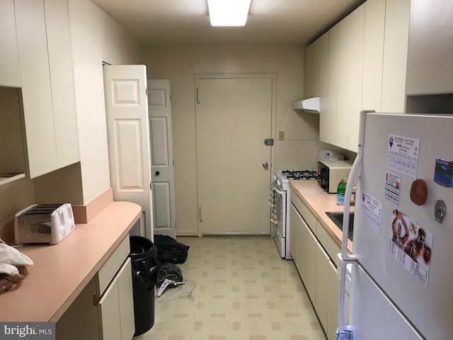 kitchen with light tile patterned floors, gas range, white refrigerator, and white cabinets