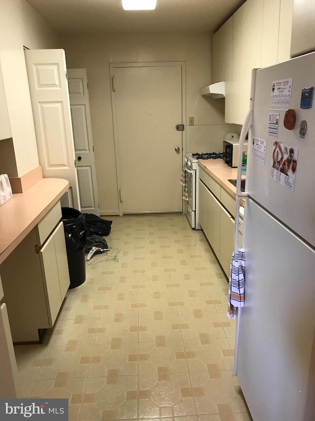 kitchen featuring gas range, light tile patterned flooring, white cabinetry, and white refrigerator