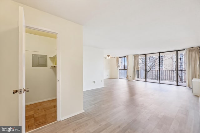 unfurnished living room featuring floor to ceiling windows, ceiling fan, light wood-type flooring, electric panel, and baseboards