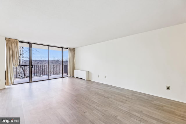 empty room featuring expansive windows, radiator heating unit, and light wood-type flooring