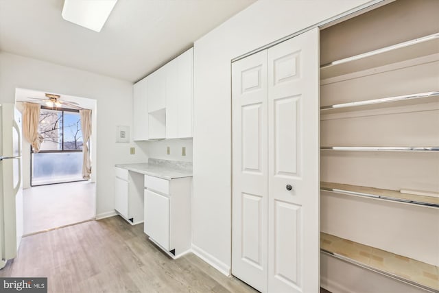 kitchen with light wood finished floors, light countertops, a ceiling fan, freestanding refrigerator, and white cabinets