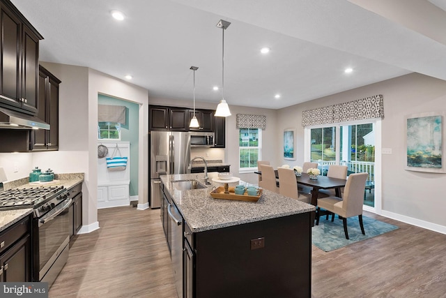 kitchen featuring a kitchen island with sink, wood-type flooring, decorative light fixtures, sink, and appliances with stainless steel finishes