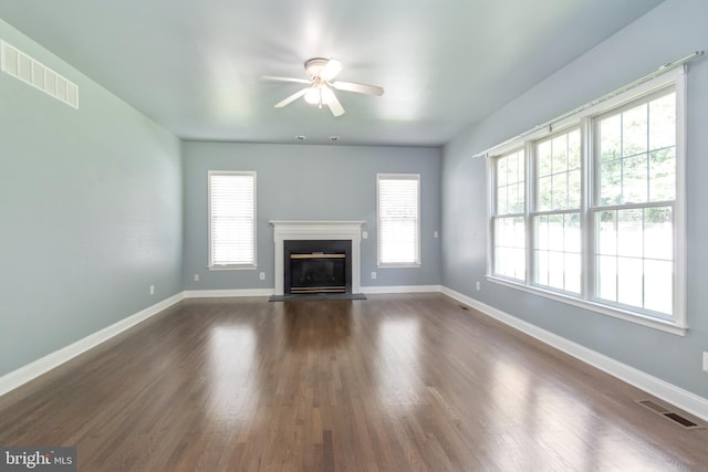 unfurnished living room with a healthy amount of sunlight, dark wood-type flooring, and ceiling fan