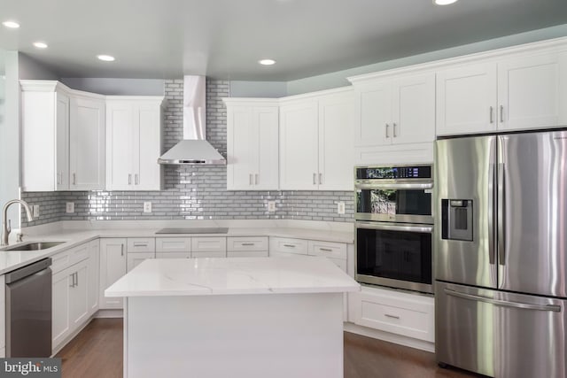 kitchen with sink, white cabinetry, a kitchen island, stainless steel appliances, and wall chimney exhaust hood