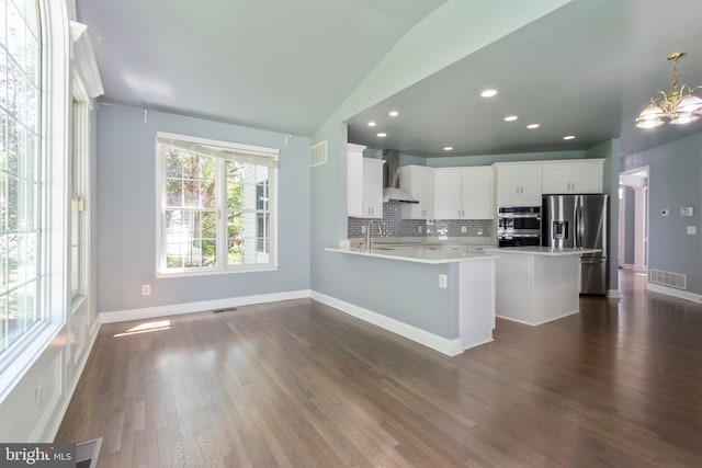 kitchen featuring wall chimney exhaust hood, stainless steel appliances, decorative light fixtures, decorative backsplash, and white cabinetry