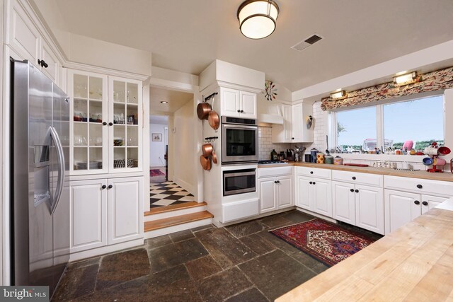 kitchen featuring wooden counters, appliances with stainless steel finishes, white cabinets, and tasteful backsplash