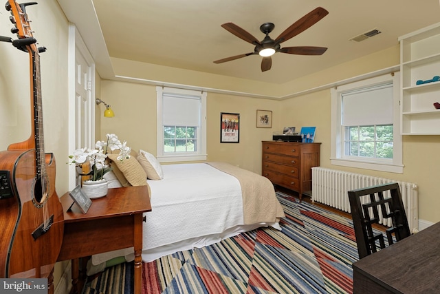 carpeted bedroom with multiple windows, ceiling fan, and radiator heating unit