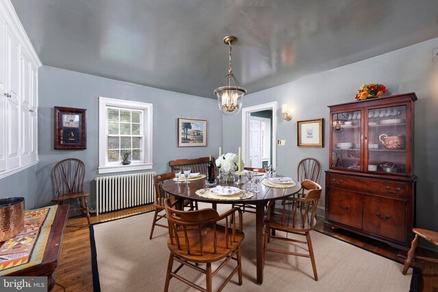 dining space with dark wood-type flooring, a notable chandelier, and radiator heating unit