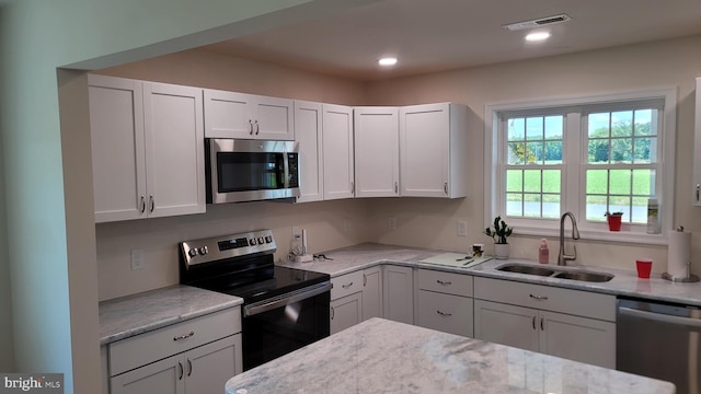 kitchen with light stone countertops, sink, white cabinets, and appliances with stainless steel finishes