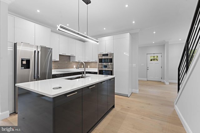 kitchen with light hardwood / wood-style flooring, hanging light fixtures, a center island with sink, sink, and white cabinetry