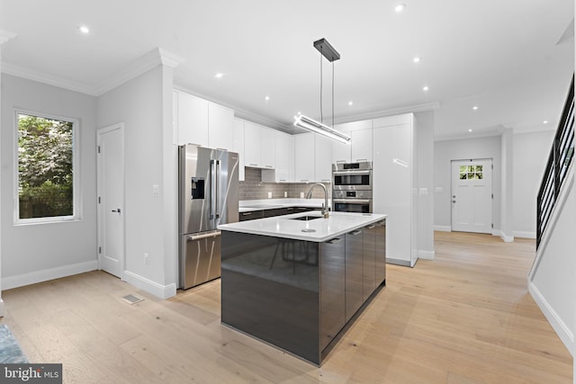 kitchen with white cabinetry, a kitchen island with sink, stainless steel appliances, light hardwood / wood-style floors, and decorative light fixtures