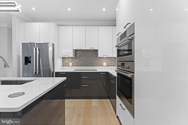 kitchen featuring appliances with stainless steel finishes, sink, backsplash, white cabinetry, and light hardwood / wood-style flooring