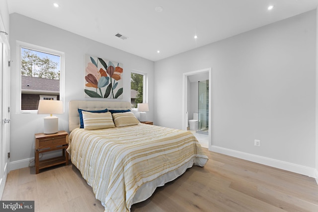 bedroom with light hardwood / wood-style flooring, multiple windows, and connected bathroom