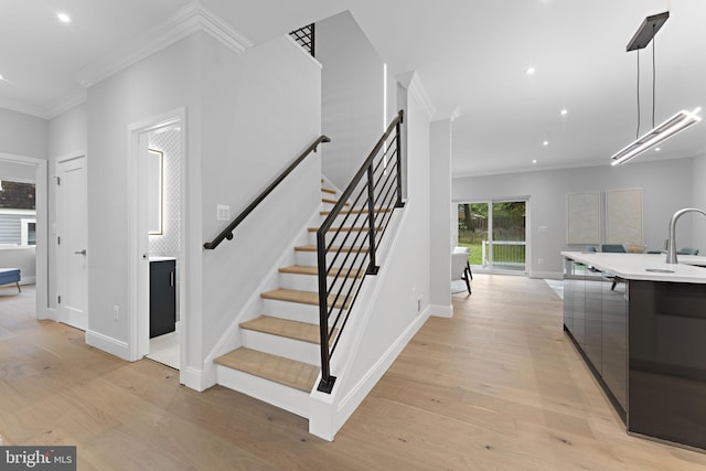 stairs featuring sink, wood-type flooring, and ornamental molding