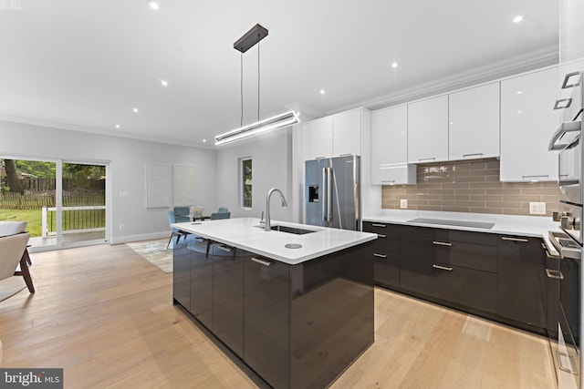 kitchen with hanging light fixtures, stainless steel appliances, sink, light wood-type flooring, and white cabinetry