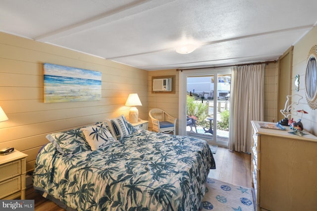 bedroom featuring light hardwood / wood-style floors, a wall unit AC, a textured ceiling, and access to outside