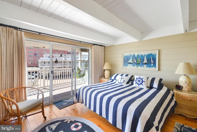 bedroom featuring access to exterior, beamed ceiling, wooden walls, and wood finished floors