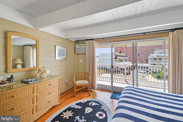 bedroom with access to outside, beam ceiling, an AC wall unit, wood walls, and light wood-type flooring