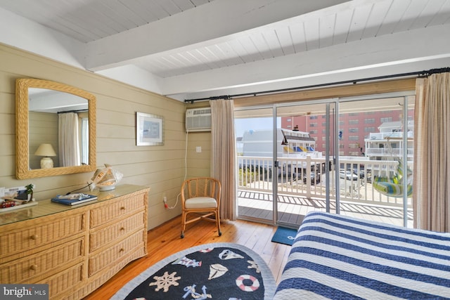 bedroom with wooden walls, a wall unit AC, light hardwood / wood-style floors, access to outside, and beamed ceiling