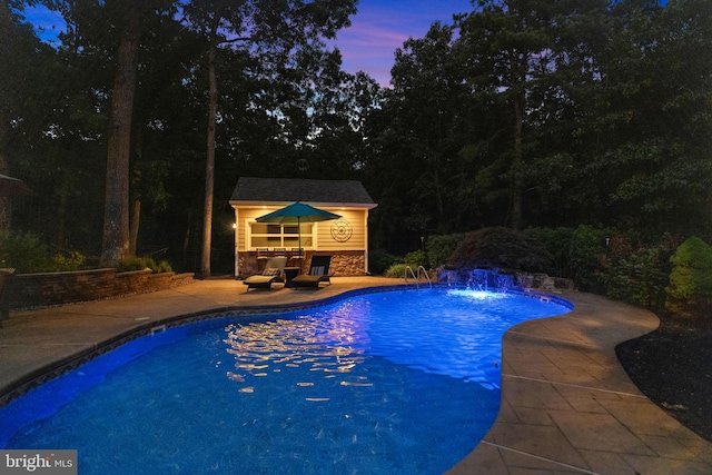 pool at dusk featuring a patio area, an outdoor structure, and pool water feature