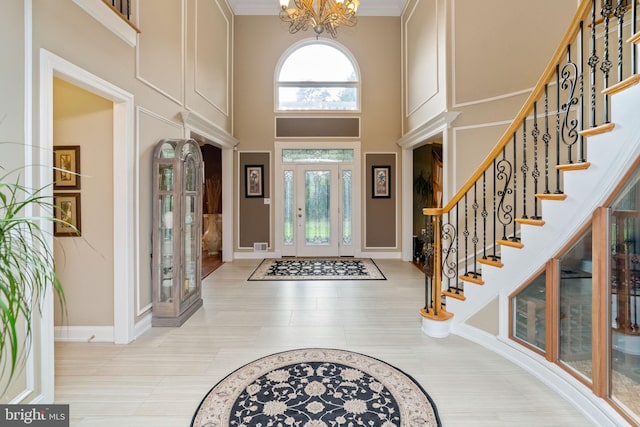 tiled entrance foyer featuring ornamental molding, an inviting chandelier, and a towering ceiling