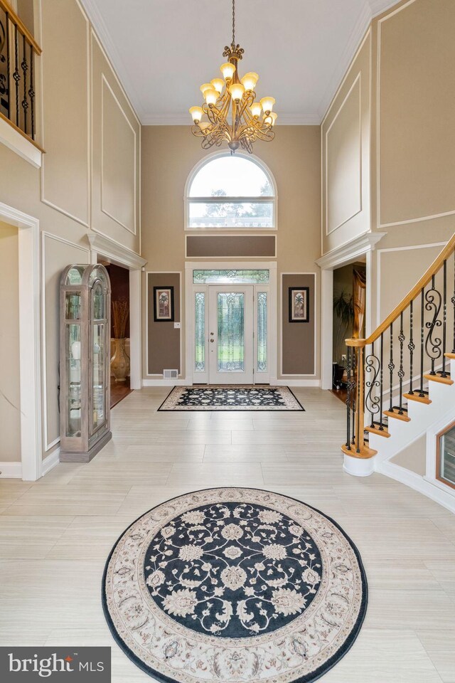 tiled foyer entrance featuring crown molding, a chandelier, and a towering ceiling