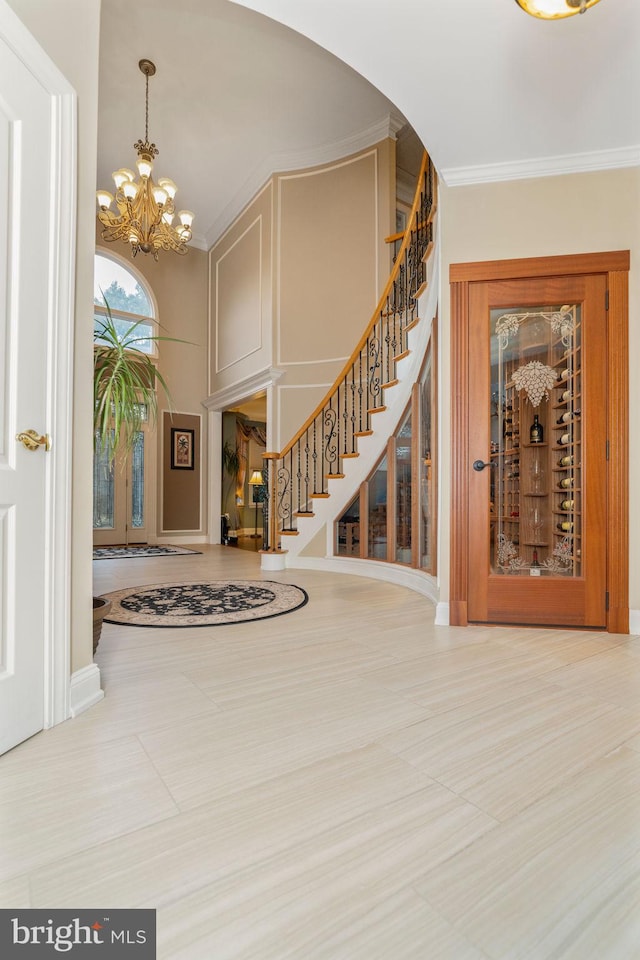 tiled foyer entrance with ornamental molding and a chandelier