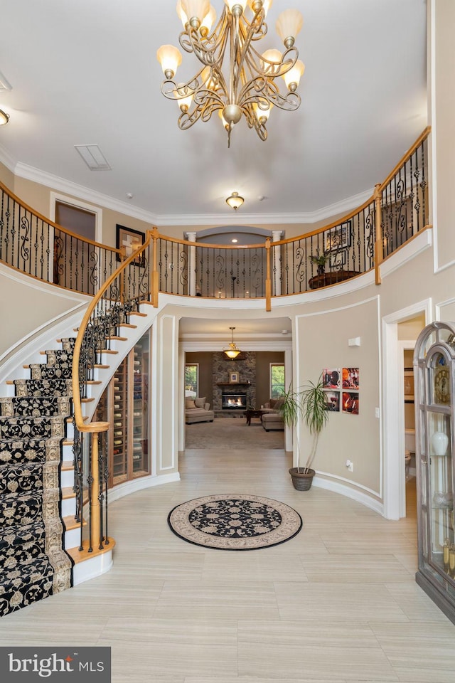 tiled foyer entrance with a towering ceiling, a fireplace, an inviting chandelier, and ornamental molding