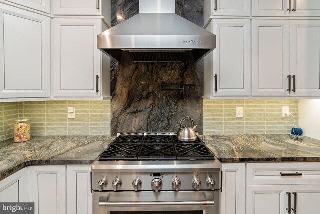 kitchen with high end range, white cabinetry, wall chimney exhaust hood, and tasteful backsplash