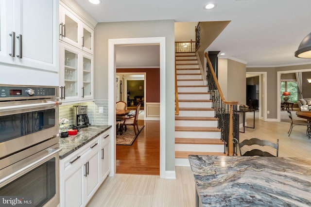 kitchen featuring light wood-type flooring, backsplash, white cabinets, crown molding, and double oven