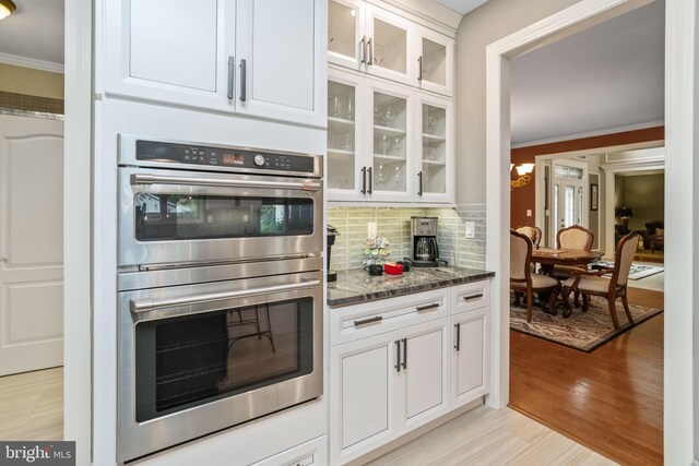 kitchen with light hardwood / wood-style flooring, ornamental molding, stainless steel double oven, white cabinets, and dark stone countertops