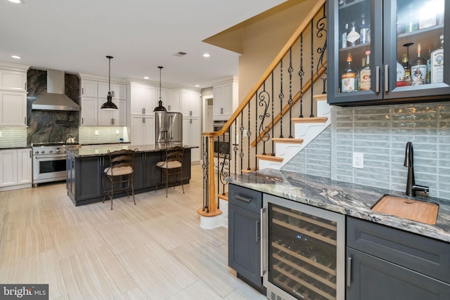 bar featuring wall chimney range hood, tasteful backsplash, white cabinets, appliances with stainless steel finishes, and wine cooler