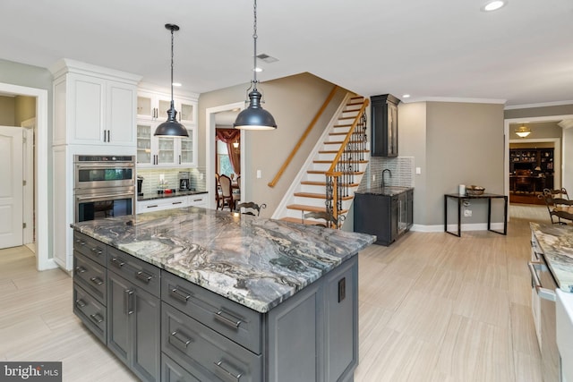 kitchen featuring tasteful backsplash, double oven, white cabinets, a center island, and hanging light fixtures