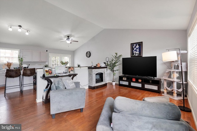 living room with wood-type flooring, a stone fireplace, vaulted ceiling, and ceiling fan