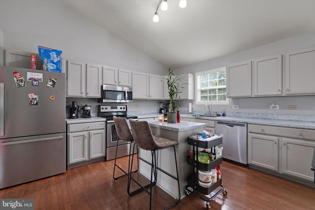 kitchen with appliances with stainless steel finishes, dark wood-type flooring, a breakfast bar area, lofted ceiling, and sink