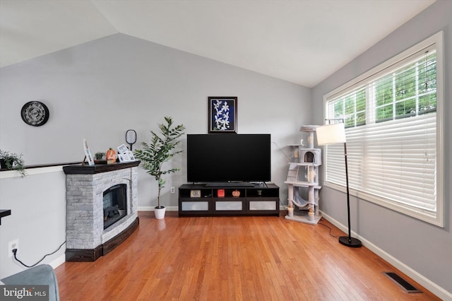 living room featuring light wood-type flooring, lofted ceiling, and a stone fireplace