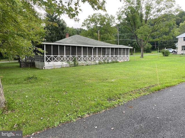 exterior space with a sunroom, roof with shingles, a yard, and a chimney