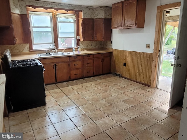 kitchen with wooden walls, sink, light tile patterned floors, and black range with electric stovetop