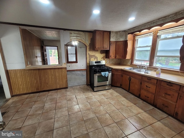 kitchen featuring light tile patterned flooring, wood walls, a textured ceiling, stainless steel gas stove, and sink