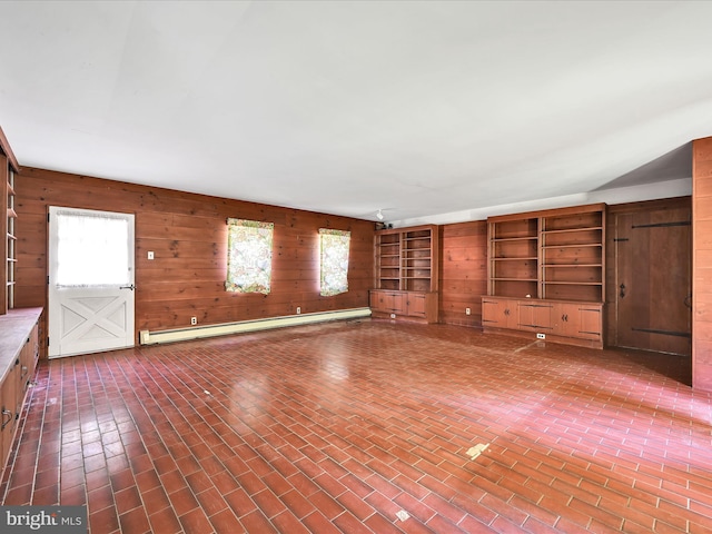 unfurnished living room featuring a wealth of natural light, wooden walls, and a baseboard heating unit