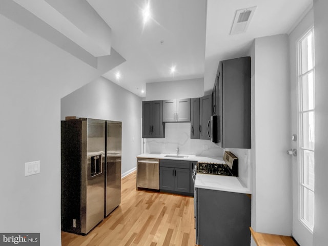 kitchen with appliances with stainless steel finishes, backsplash, gray cabinets, light hardwood / wood-style flooring, and sink