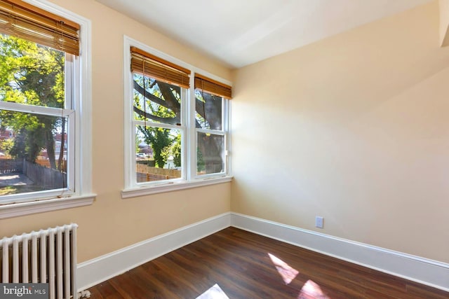 empty room featuring dark hardwood / wood-style floors, a healthy amount of sunlight, and radiator