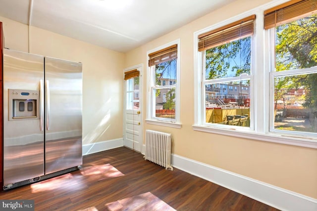 interior space with radiator heating unit, stainless steel fridge, dark wood-type flooring, and a healthy amount of sunlight