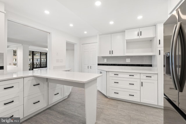 kitchen with backsplash, kitchen peninsula, stainless steel fridge, and white cabinets