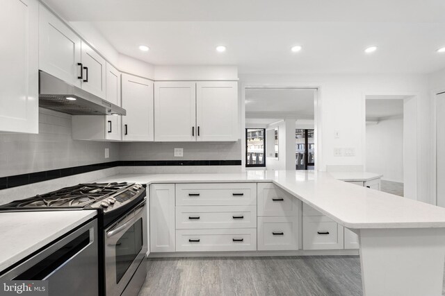 kitchen with light hardwood / wood-style floors, white cabinetry, kitchen peninsula, appliances with stainless steel finishes, and tasteful backsplash